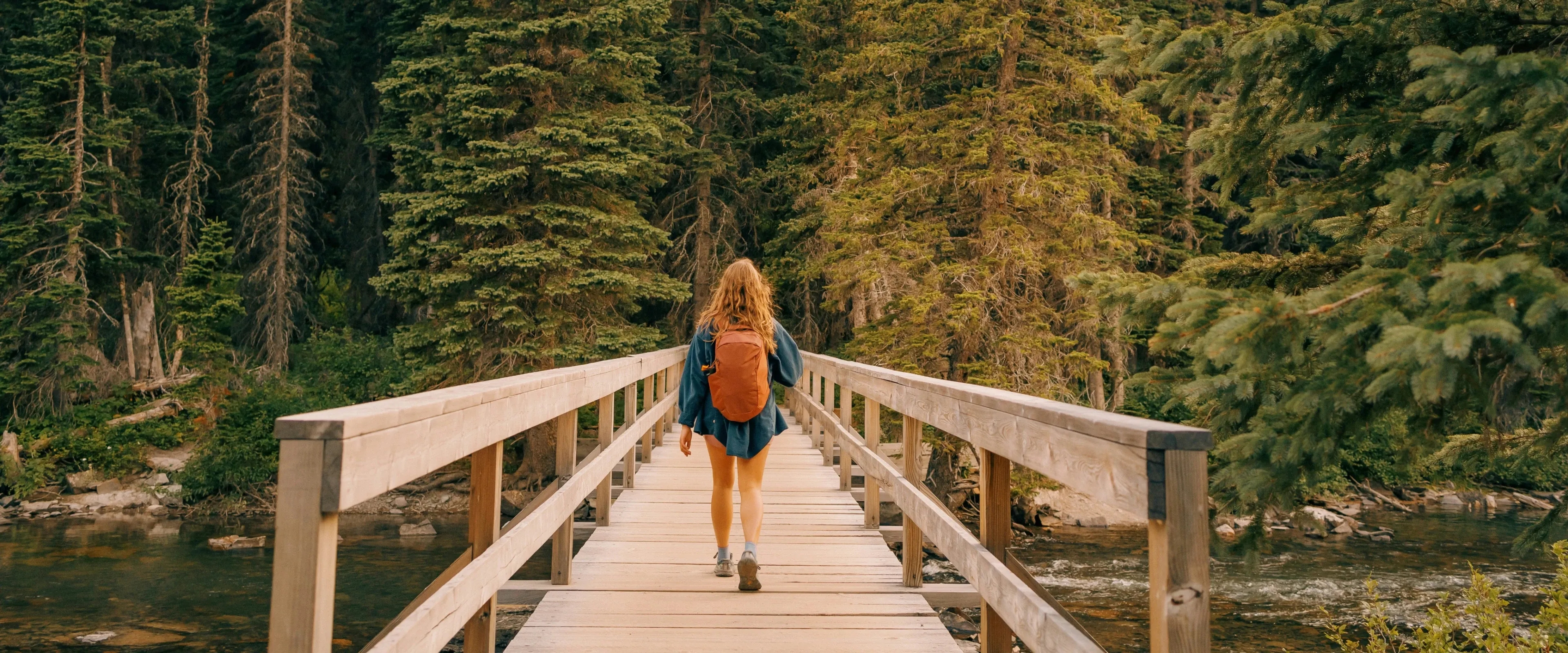 Woman with a backpack walks down a pier among the trees